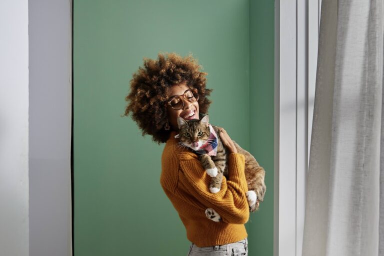 does my cat love me: a tabby cat in a checkered scarf is being held by his pet parent mom in their living room with a green wall in the background.