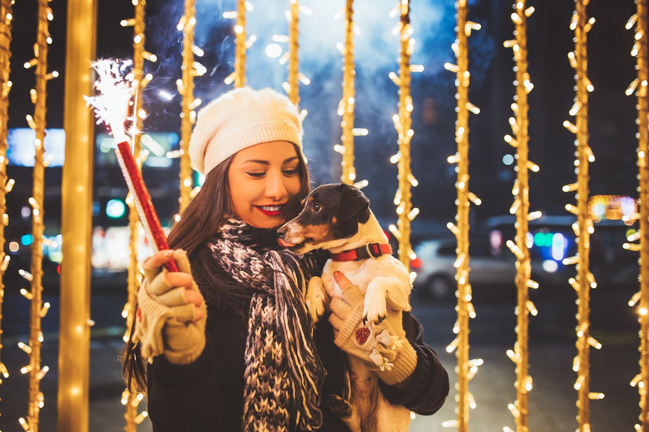 A woman holding a firework and a small dog in front of New Years Even decorations