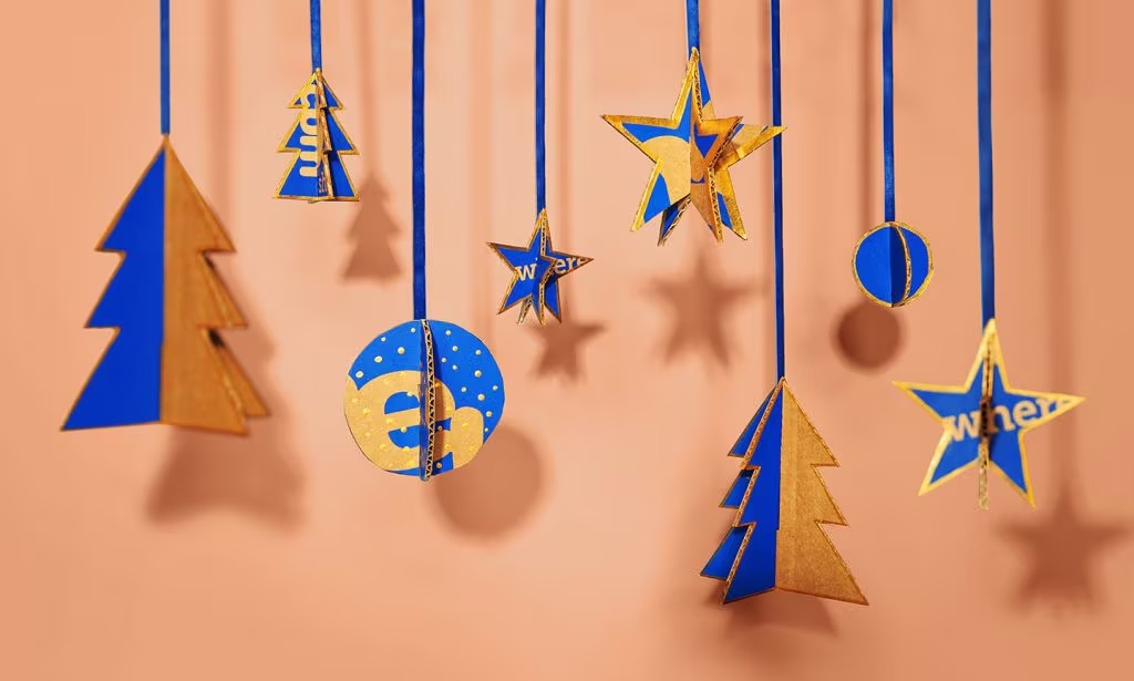 Photo of Christmas ornaments made from Chewy boxes hanging in front of a peach-colored backdrop