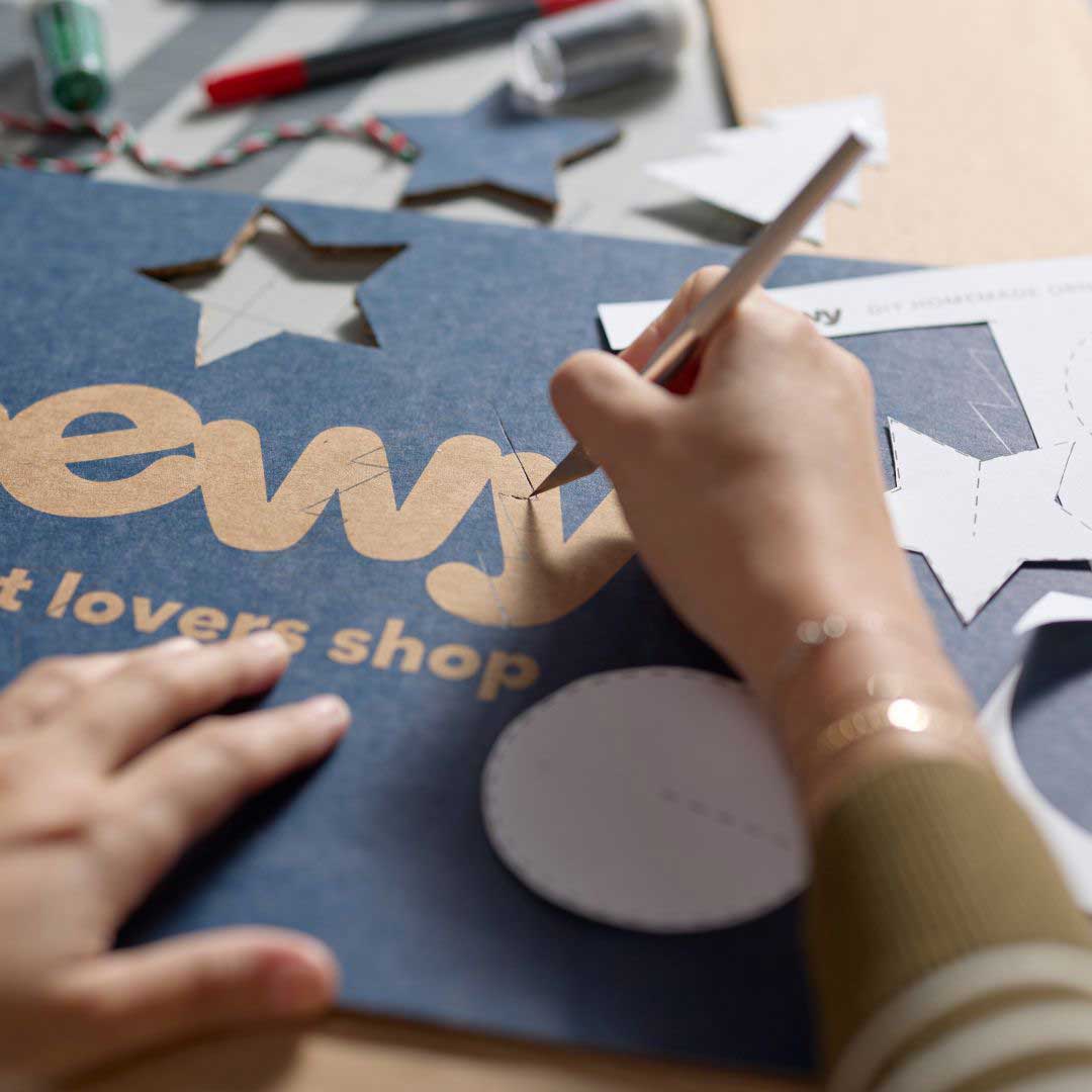 Photo of hands using a craft knife to cut DIY Christmas ornament shapes out of Chewy boxes