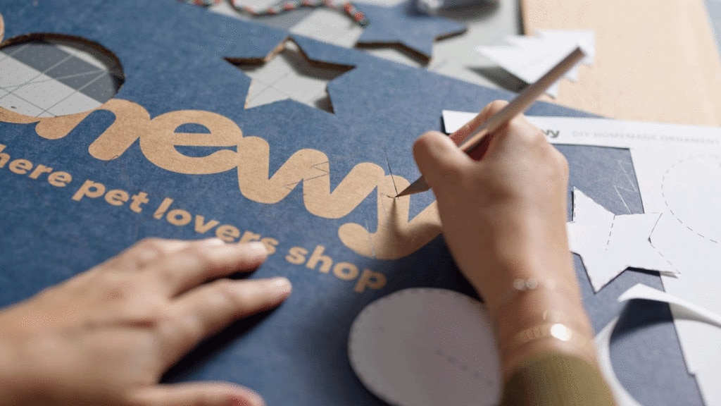 Hands cutting out pieces of a Chewy cardboard box to make a DIY Christmas tree ornament