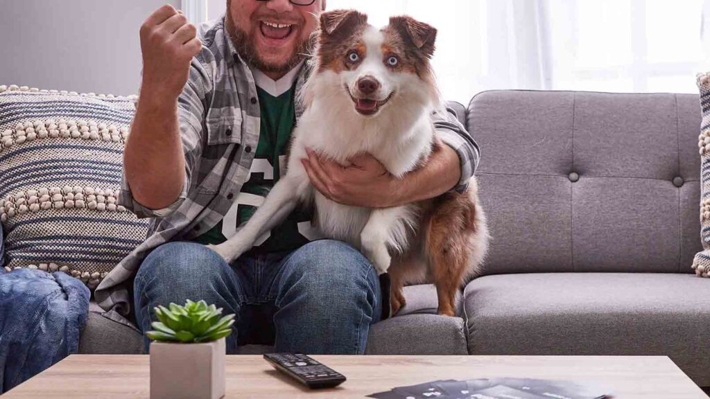 Photo of a man and his dog sitting on a couch watching a football game