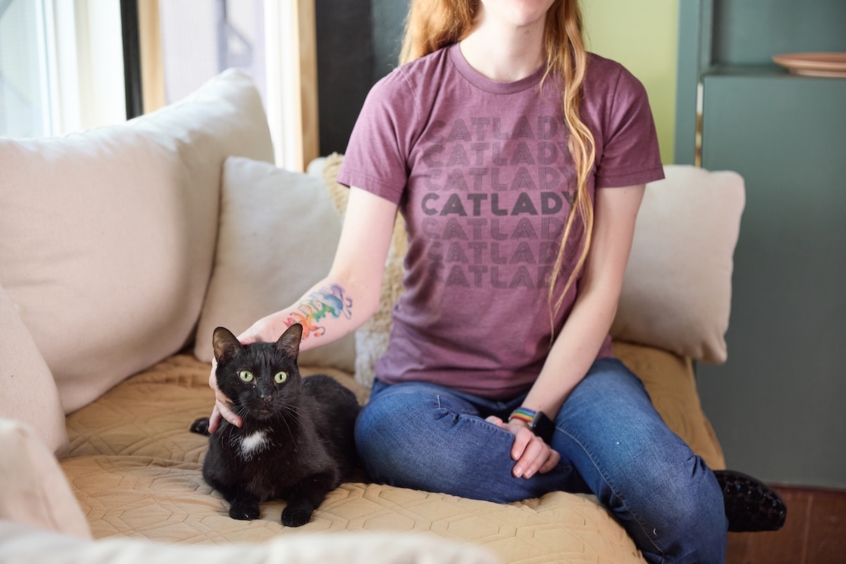 A woman sitting on a couch and petting a black cat