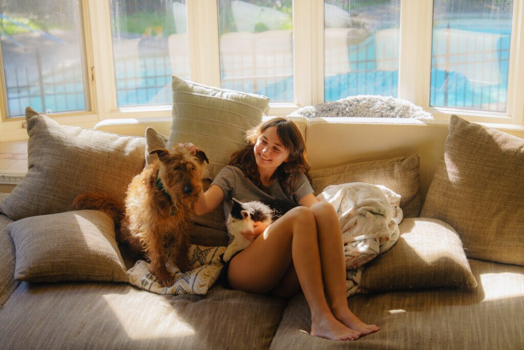 why pets need year-round heartworm prevention; woman sits on couch with dog and cat