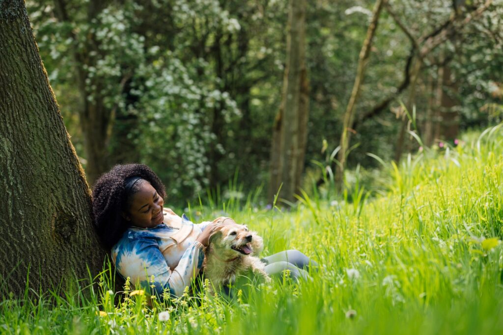 pollen allergies in dogs; a pet parent and her dog sits beneath a tree.