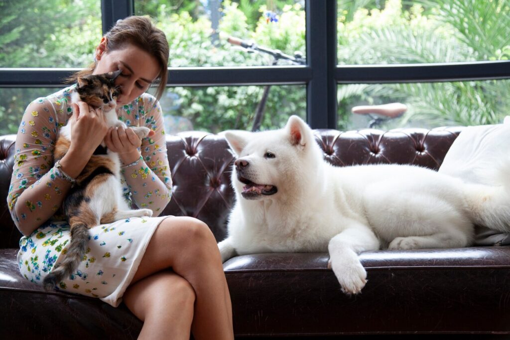 woman sitting with a fluffy white dog and calico cat on a couch