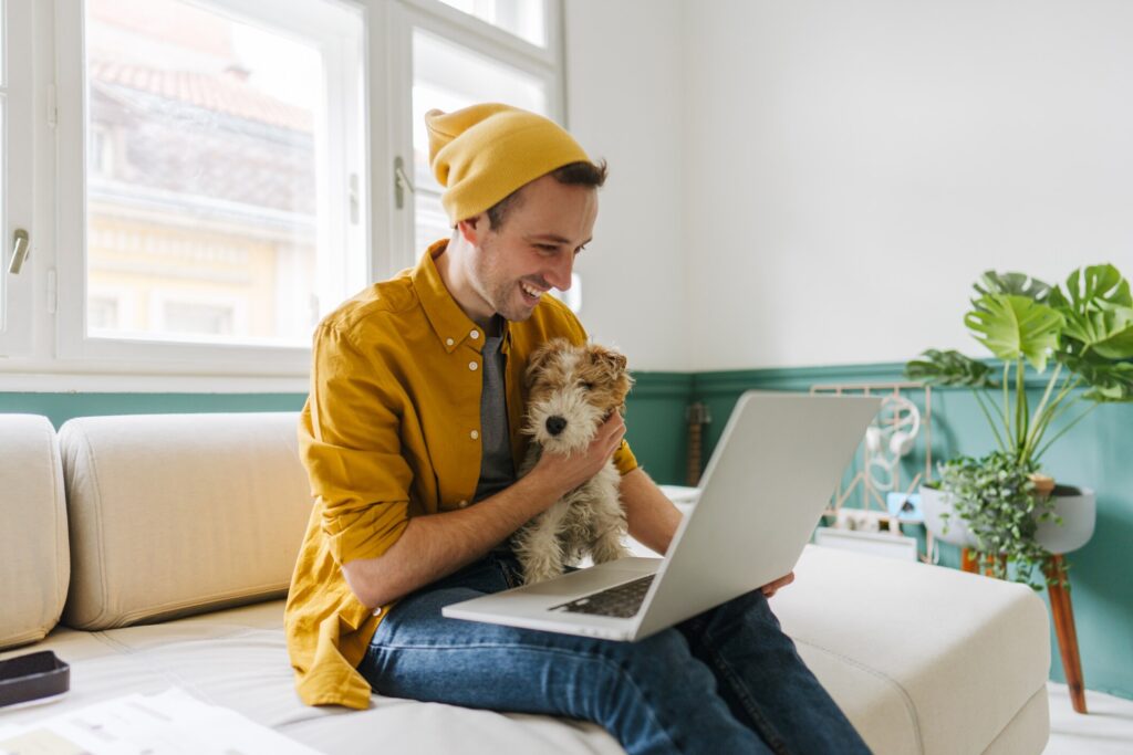 man sitting on couch with dog looking at laptop