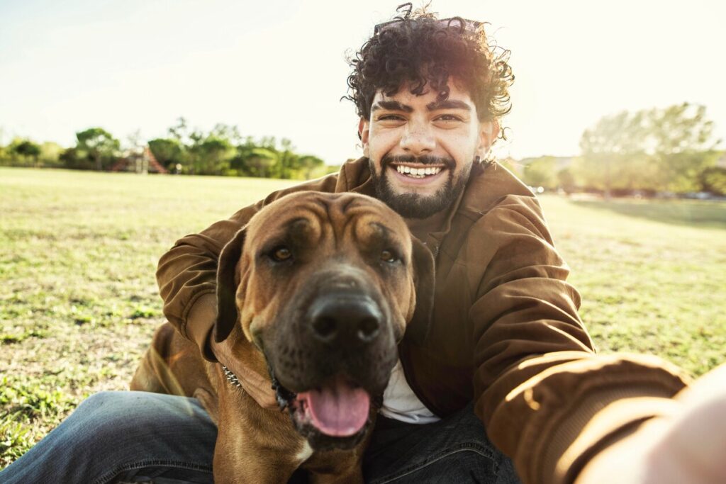 man-sitting-in-grass-with-dog-taking-selfie