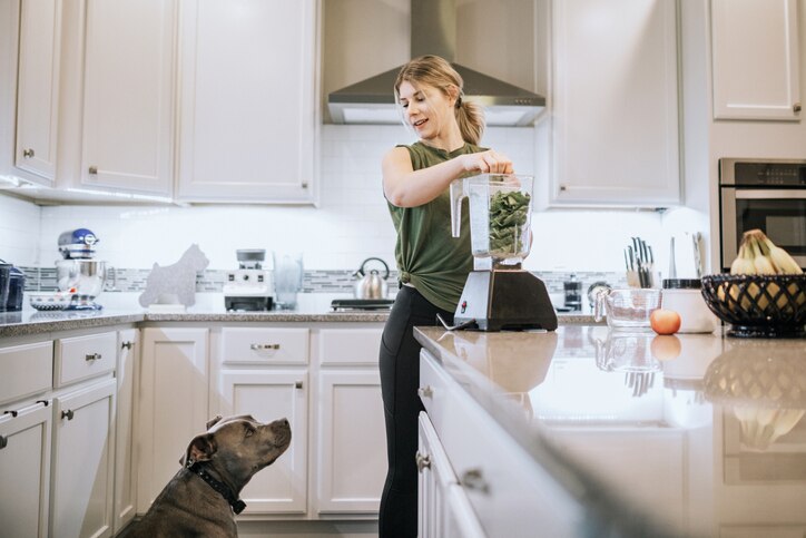 woman blending leafy greens while her dog watches