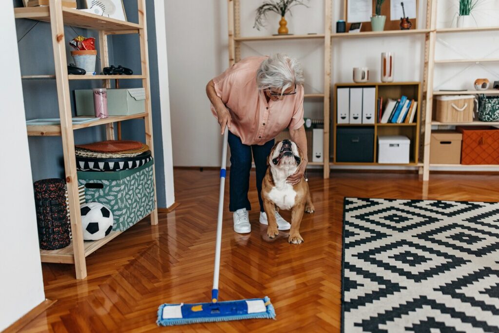 older woman petting her bulldog while vacuuming