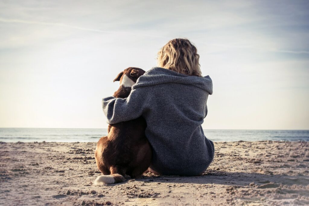 blonde woman sitting on beach hugging dog.