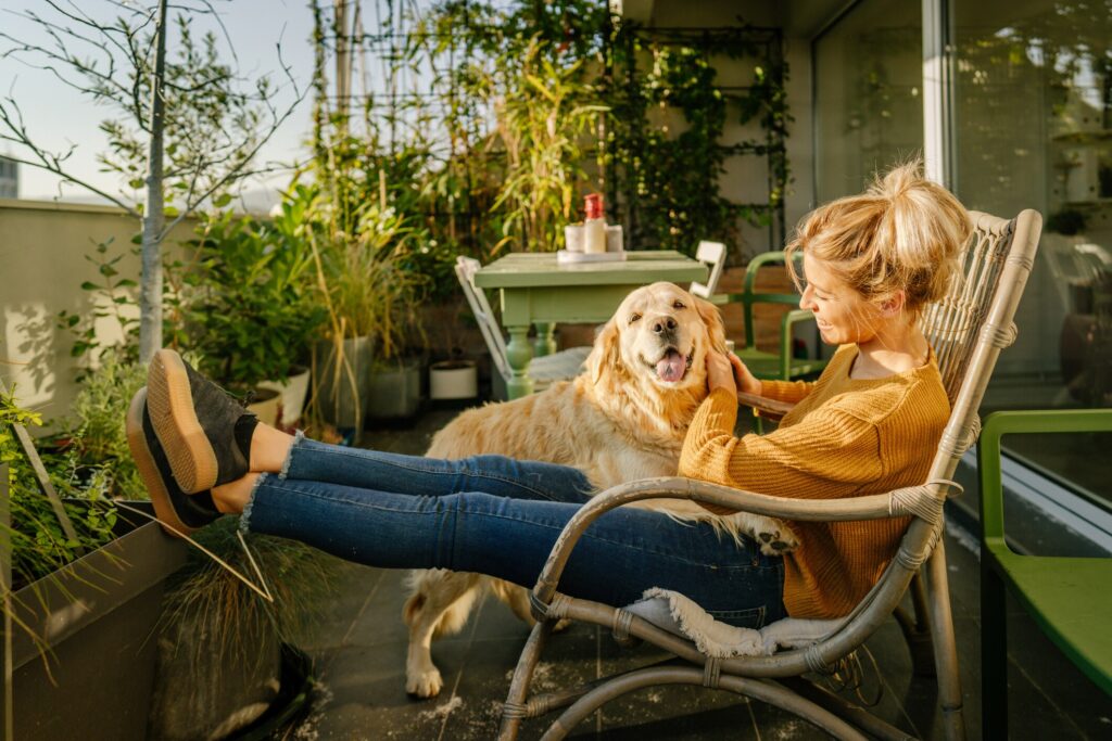 A pet parent and their Golden Retriever sit on a balcony filled with plants.