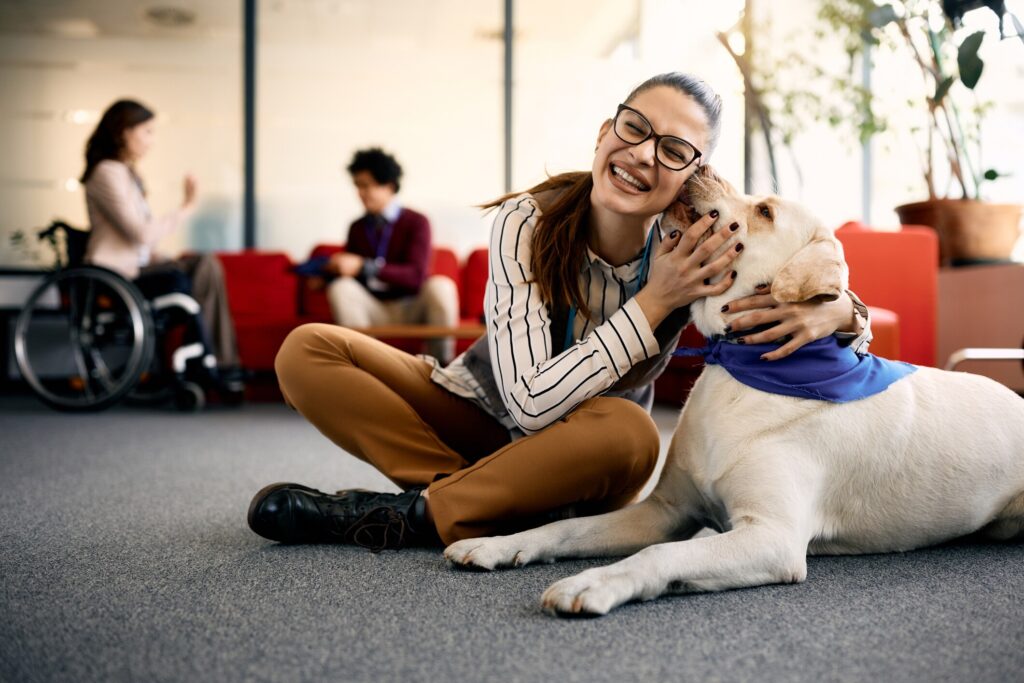 therapy dog sitting on office floor licking woman's face