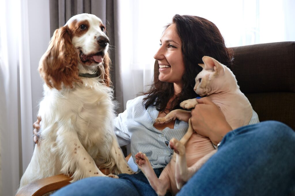 woman sits on couch holding cat and dog.