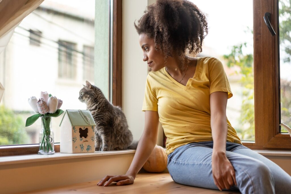 woman sitting with her gray tabby cat and looking out a window