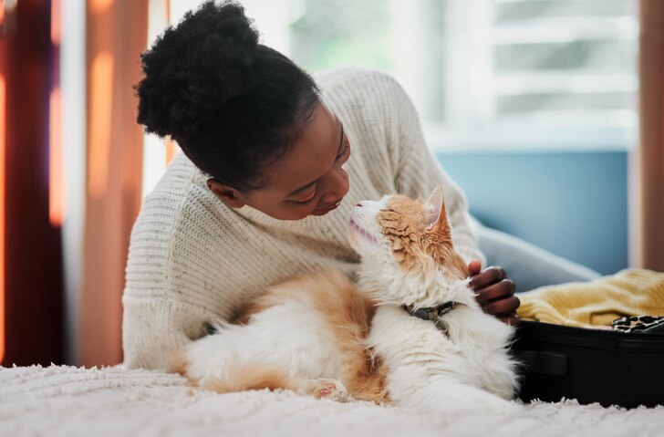 A woman leaning over and petting her fluffy orange and white senior cat.