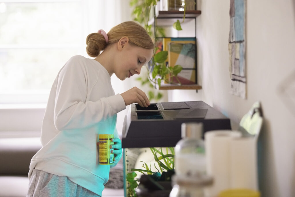 woman fills fish tank feeder in her home aquarium