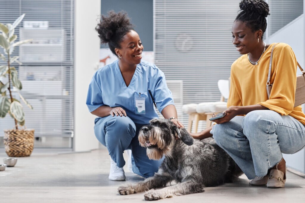 an African American woman and her dog chat with a vet doctor in a clinic waiting room before an appointment.