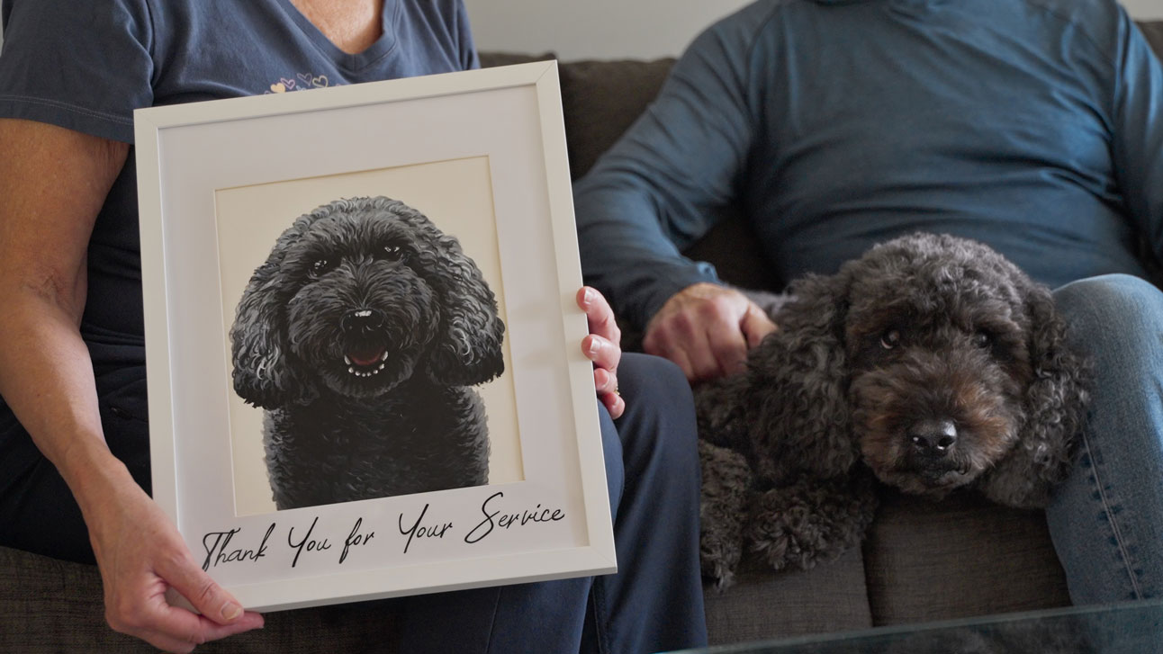 Taylor lays in her pet parent's lap beside an illustrated portrait of her with the words "Thank You For Your Service"