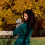 A woman holding a Russian Blue cat outside during autumn