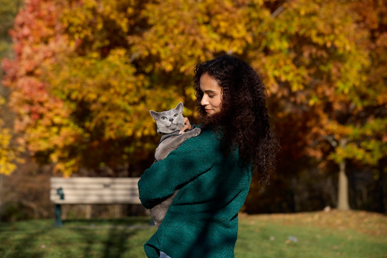 A woman holding a Russian Blue, a hypoallergenic cat, outside during autumn