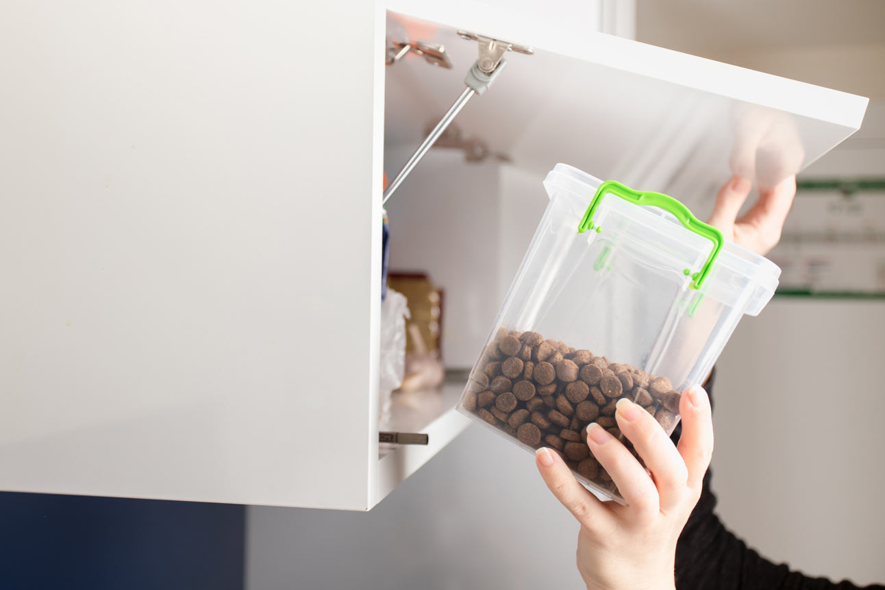 Hands taking a plastic pet food storage bin down from a shelf
