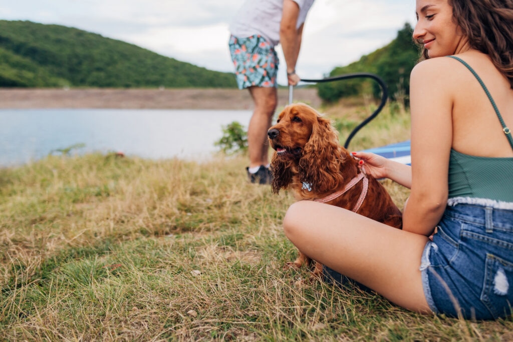 woman sitting in front of lake holding dog by harness.