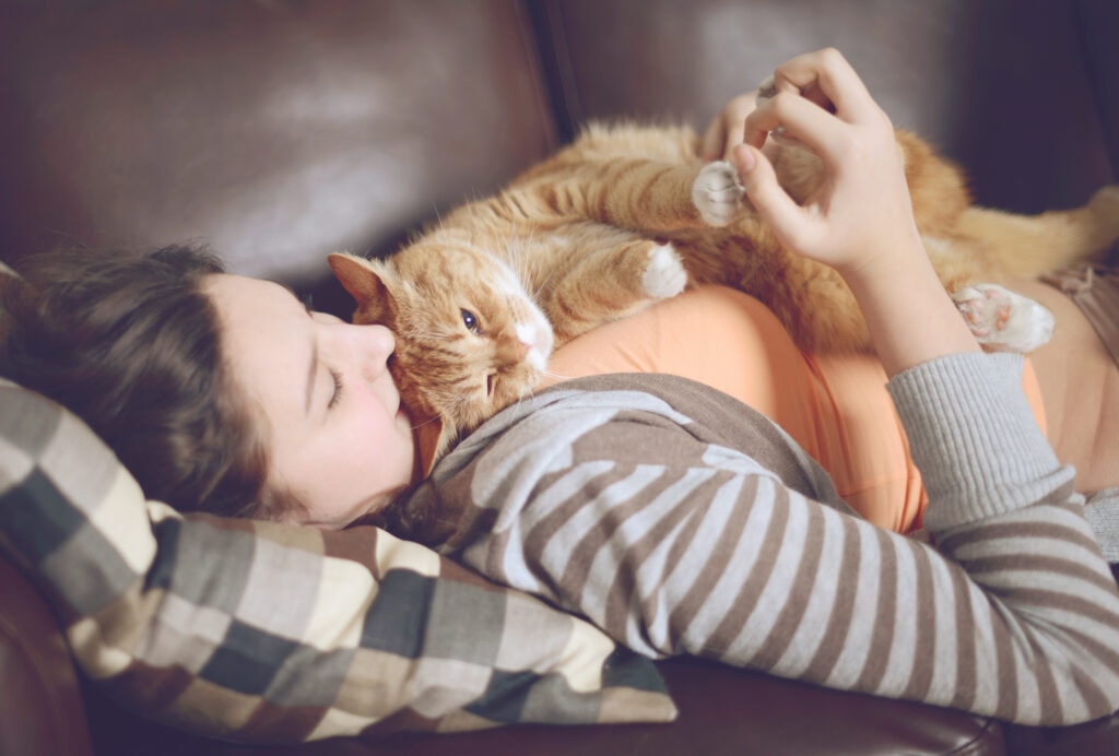 a girl lying on a couch with a ginger cat lying across her chest