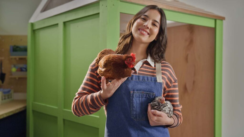 A woman holding chickens in front of a DIY chicken coop