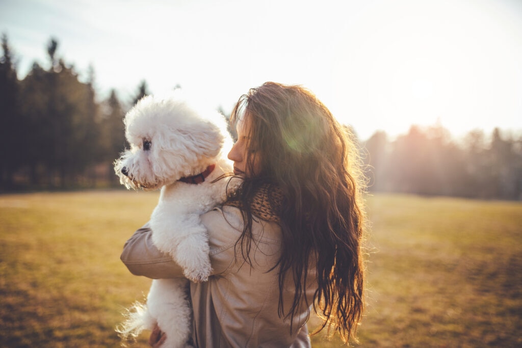 woman holding a white fluffy dog in a field