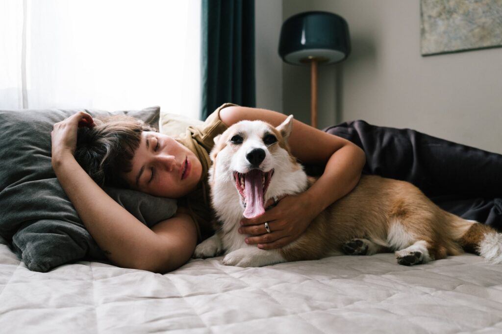 Do dogs know when you’re sick? A woman snuggles her corgi in bed.