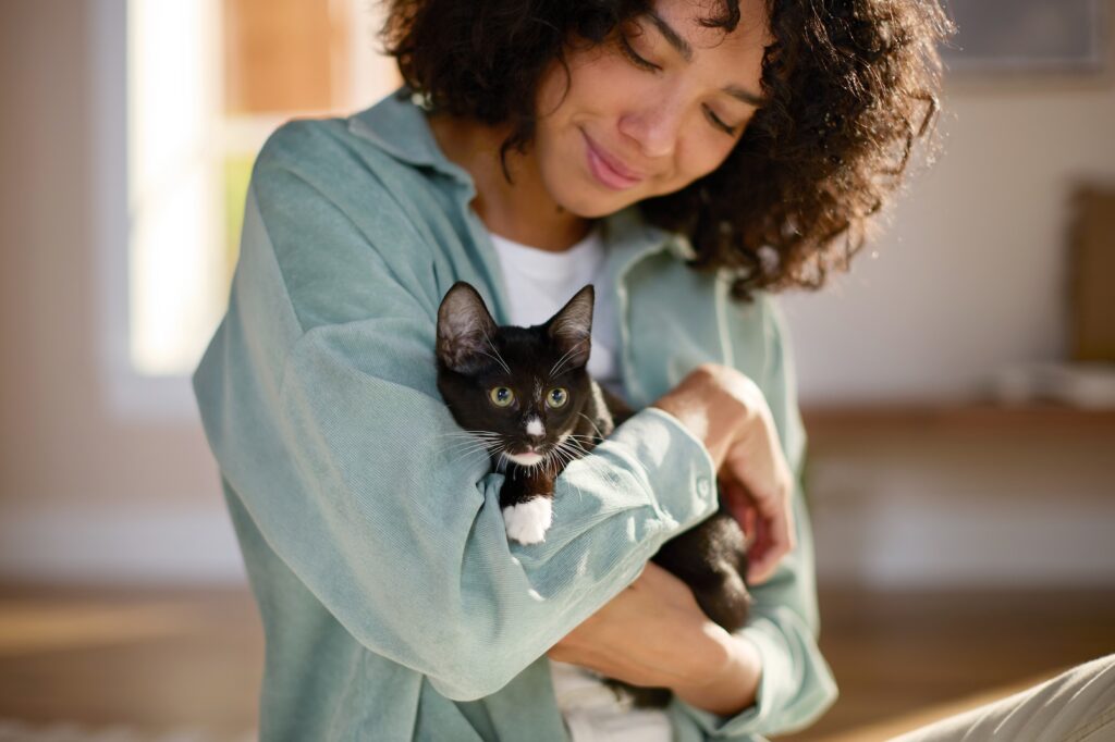 A woman holds and smiles down at a black and white kitten.